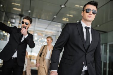 bodyguards protecting privacy of female clients, mother and daughter walking out of hotel on blurred background, personal safety of rich family, men in sunglasses and suit on duty  clipart