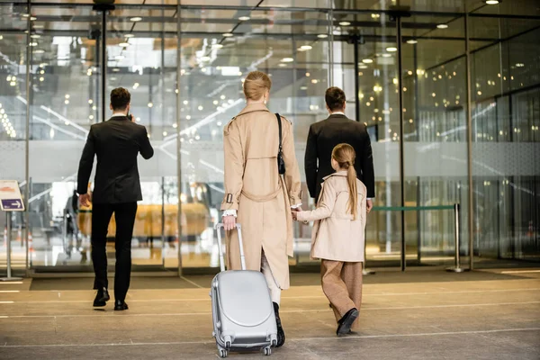 個人の安全保障 金髪の女性と未成年の子供の隣を歩く2人のボディーガード ホテルに入る 娘と手を携えている母親 安全と保護 バックビュー — ストック写真