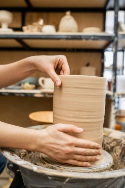 Cropped view of hands of craftswoman making clay vase on pottery wheel in workshop clipart