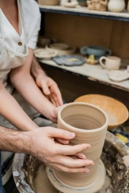 Cropped view of couple in love making clay vase together on pottery wheel in ceramic workshop clipart