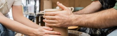 Cropped view of artisans making clay vase on pottery wheel in ceramic workshop, banner clipart
