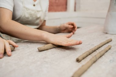 Cropped view of craftswoman in apron shaping clay near boyfriend in ceramic workshop clipart