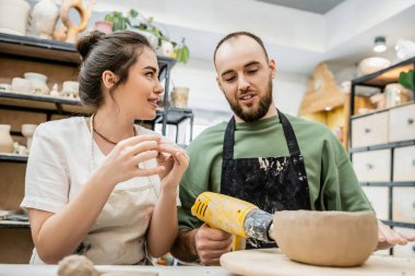 Zanaatkar ısıtıcı ile toprak donanımı kurutuyor ve seramik atölyesinde killi kız arkadaşıyla konuşuyor.