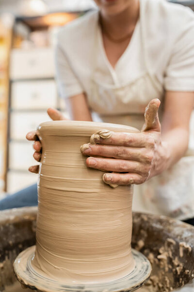 Cropped view of female african in blurred apron shaping clay on pottery wheel in ceramic workshop
