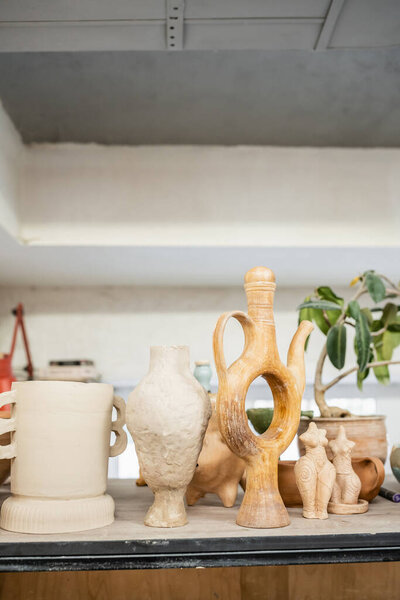 Different clay sculptures on rack near green plant in ceramic workshop
