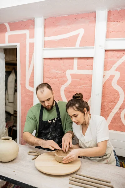 stock image Couple of sculptors shaping clay bowl while working together in ceramic workshop