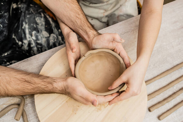 Top view of couple of sculptors making clay bowl together in ceramic workshop
