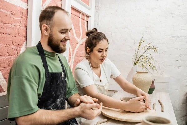 stock image Craftswoman in apron talkig to boyfriend and shaping clay bowl in ceramic workshop