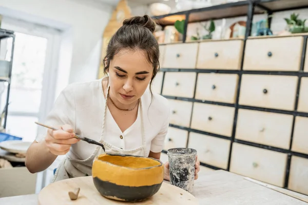 Brunette Pengrajin Wanita Apron Mewarnai Mangkuk Keramik Saat Bekerja Studio — Stok Foto