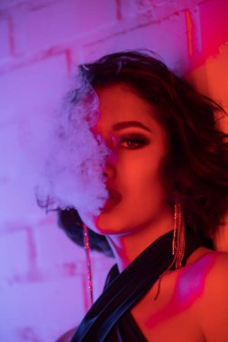 Modayı takip eden Asyalı genç bir kadının portresi. Gece kulübünde neon ışıkta duman çıkarıyor.