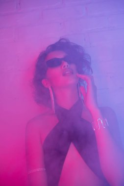 Güneş gözlüklü seksi Asyalı kadın. Gece kulübünde duman ve neon ışıkla poz veriyor.