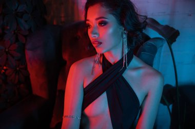 Gece kulübünde neon ışıkta bitkilerin yanından uzaklaşan seksi Asyalı kadın portresi.