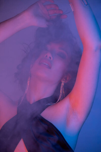 Модная юная брюнетка азиатка, танцующая в дыму и неоновом свете в ночном клубе