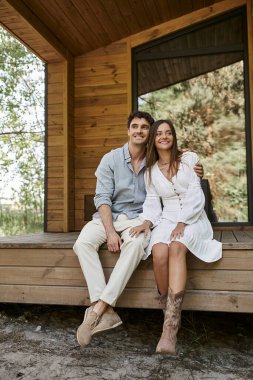Tatil evi, yaz aşkı, güzel bir kadına sarılıp verandada oturan mutlu bir çift.