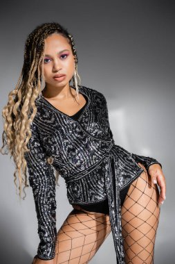 Gri arka planda poz veren seksi balıkçı taytlı baştan çıkarıcı kadın, Afro-Amerikan tarzı, cesur.