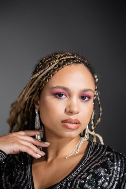 Lüks takılar takmış Afrikalı Amerikalı kadın portresi gri arka planda kameraya bakıyor, parti