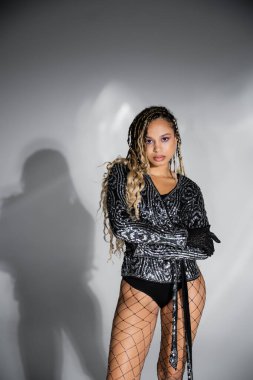 Kendine güvenen ve seksi, esmer tenli kolları katlanmış, gri arka planı olan, cesur bir kadın.