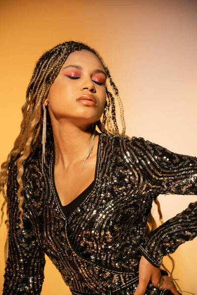 attractive african american woman with closed eyes posing in cocktail dress on yellow, bold makeup