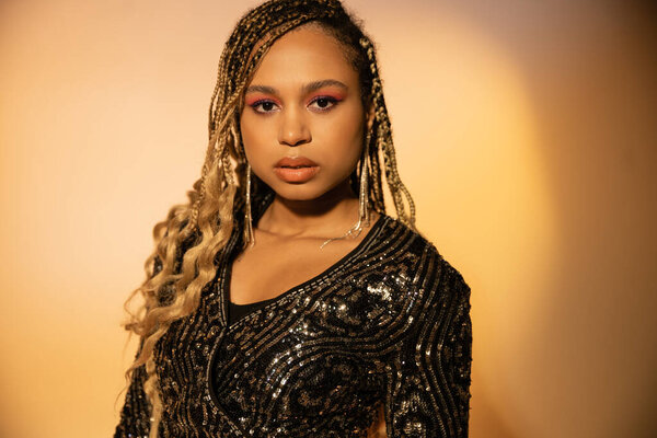 portrait of attractive african american woman looking at camera, posing in cocktail dress on yellow