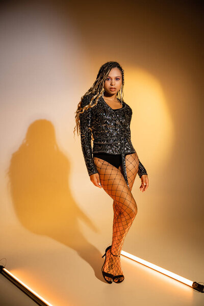 sexy african american woman standing in fishnet tights and high heels on yellow background, style