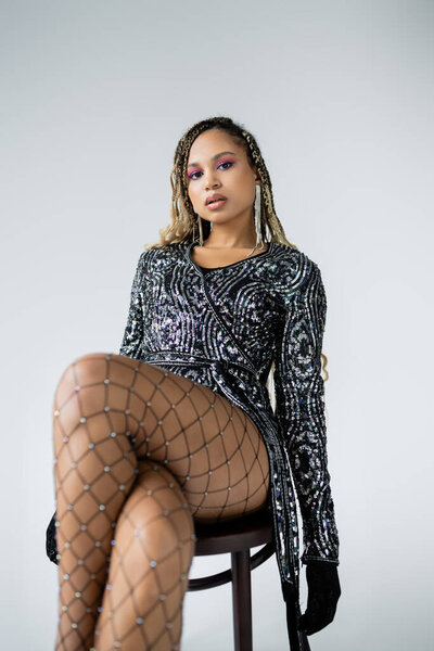 fashion, seductive african american woman sitting on chair, fishnet tights and high heels, party