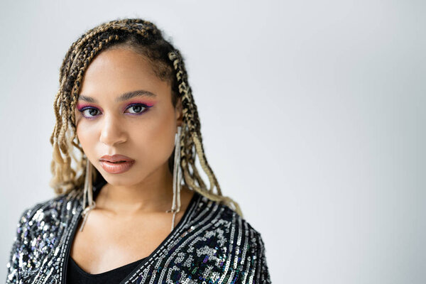 portrait of african american woman looking at camera on grey background, bold makeup, earrings