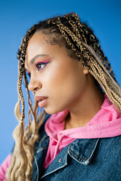 portrait of beautiful dark skinned woman with dreadlocks looking at camera on blue background