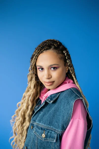 Çekici Afro-Amerikalı kadın pembe kapüşonlu ve kot ceketli mavi arka planda, koyu tenli