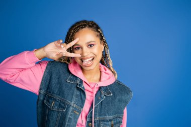 Mutlu Afro-Amerikalı kadın elinde Ziyaretçi işareti, mavi üzerine dilini çıkartıyor.