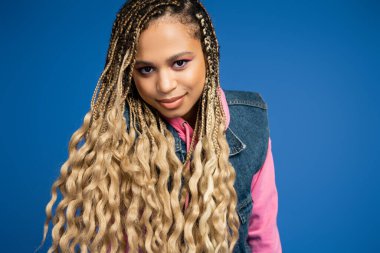 charming african american woman with dreadlocks and long hair looking at camera on blue background clipart