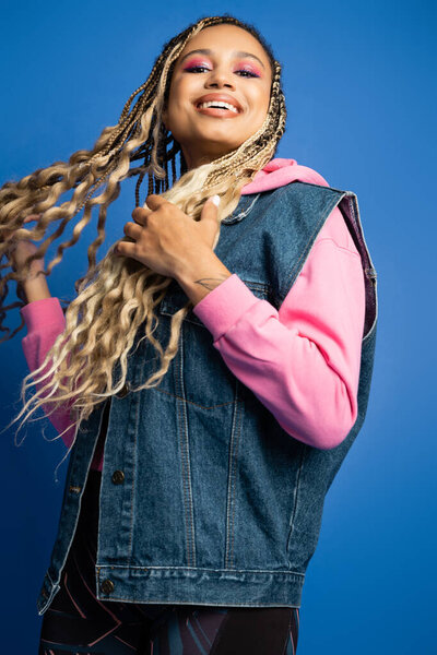 low angle view, african american woman with dreadlocks smiling and looking at camera on blue