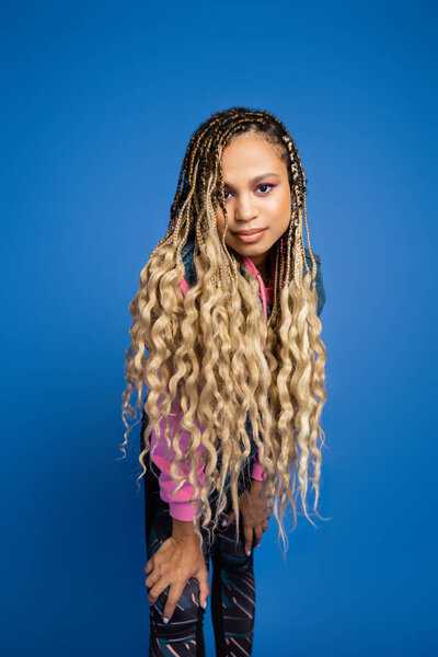 beautiful african american woman with dreadlocks and bold makeup looking at camera on blue