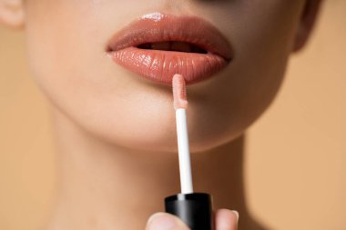 Bej üzerine izole edilmiş makyaj yaparken dudak parlatıcısı süren genç bir kadının yakın görüntüsü