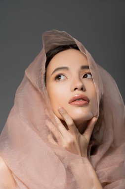 Gri üzerine izole edilmiş bej bezle poz veren Asyalı genç bir kadının portresi.