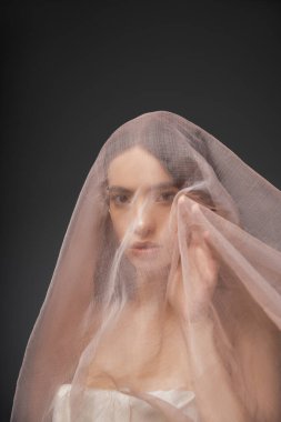 Siyah üzerine izole edilmiş bej kumaş altında poz verirken kameraya bakan Asyalı genç bir model.