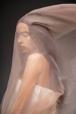 Siyah üzerine izole edilmiş bej kumaşın altında duran kapalı gözlü güzel Asyalı modelin portresi