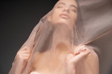 Siyah üzerinde tek başına dururken bej kumaşın altında poz veren Asyalı model portresi