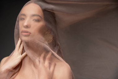 Siyah üzerine izole edilmiş bej kumaşa dokunan çıplak omuzlu kendinden emin genç Asyalı kadın.