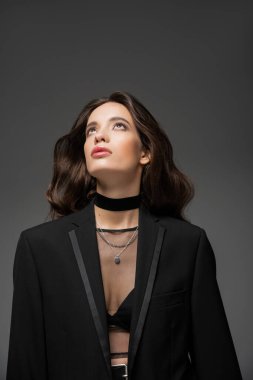 Genç ve şık Asyalı kadın portresi. Ceketli ve örgülü bluzlu. Gri üzerinde tek başına duruyor.