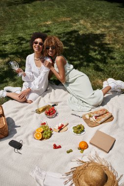 Parkta taze meyve ve sebzelerin yanında Afrikalı Amerikalı kız arkadaşların yaz pikniği.