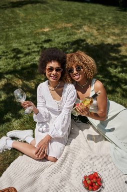 Neşeli Afrikalı Amerikalı kız arkadaşlar, beyaz elbiseler, şarap şişesi, bardak, yaz pikniği