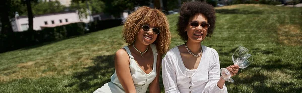 summer picnic, happy african american woman with wine glasses near stylish girlfriend, banner