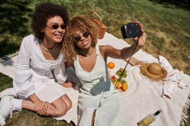Kaygısız Afrikalı, güneş gözlüklü Amerikalı kız arkadaşlar klasik kamera, piknik, afiş ve selfie çekiyorlar.