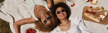 Piknik sırasında battaniyeye uzanmış mutlu Afro-Amerikalı kız arkadaşların üst görüntüsü.