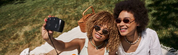 счастливые африканские американские девушки обнимаются и фотографируются на винтажную камеру в летнем парке