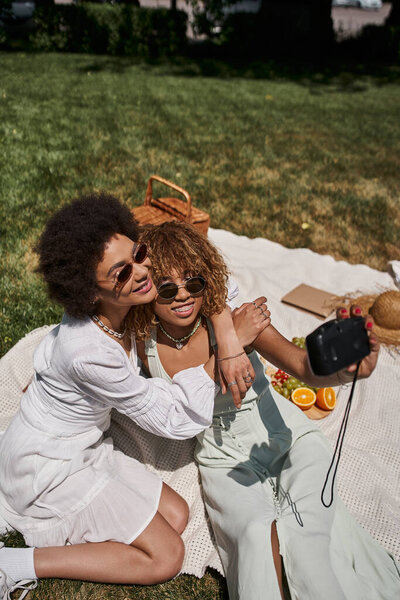 Африканская американка обнимает подружку, делает селфи на винтажную камеру, летний отдых