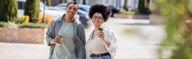 Afro-Amerikan çift ellerinde kahve ile bulanık şehir caddesinde yürüyorlar.
