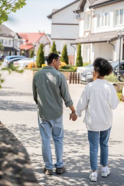 smiling african american man holding hand of girlfriend with takeaway coffee while walking outdoors clipart