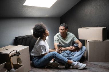Kahveli Afro-Amerikan kadın yeni evdeki tavan arası kutularının yanında erkek arkadaşıyla konuşmaya gitti.