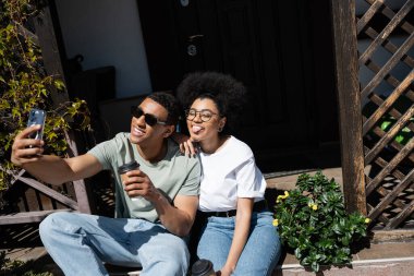 Kahveli Afro-Amerikan çift yeni evin verandasında akıllı telefondan selfie çekiyorlar.